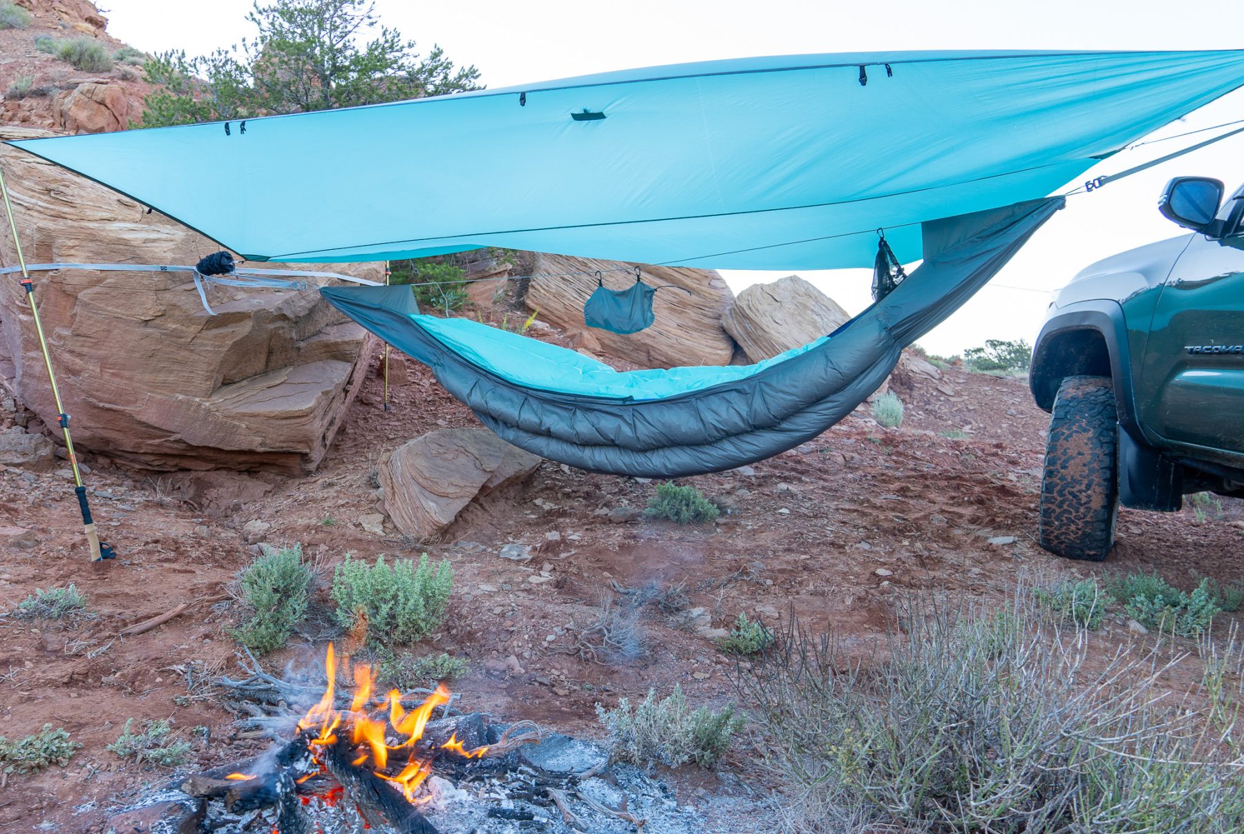 Dark blue and teal hammock set up by a fire.